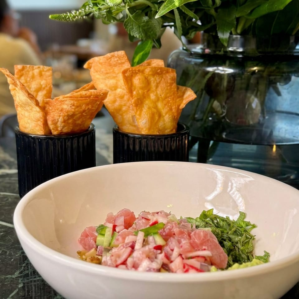 Restaurant table featuring a bowl of diced tuna with vegetables, crispy chips, leafy centerpiece, and a lit candle.